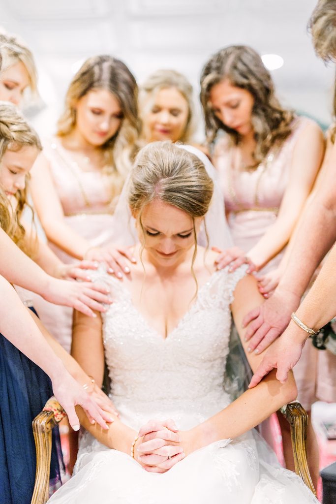 bridesmaids praying over bride
